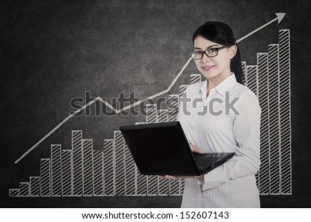 Beautiful female medical student holding laptop with bar chart background