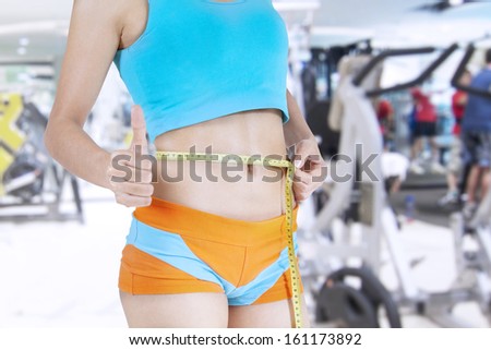 Fitness female body with measuring tape and showing thumbs up