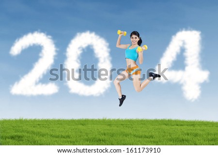 Happy fitness woman jumping with shaped clouds of new year 2014
