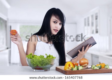 Young woman reading recipe cooking book preparing salad in the kitchen