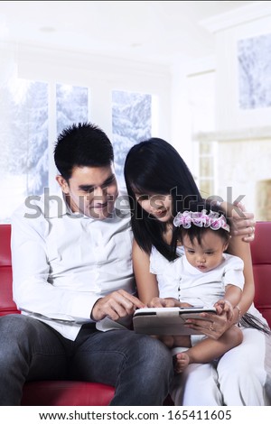 Happy family holding a digital tablet sitting on red couch
