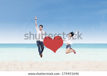 Asian couple jumping with heart card at the beach