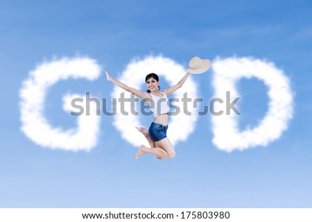 Religious  woman is jumping in front of the cloud word which says GOD