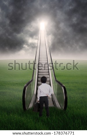 Business kid is at escalator looking at dark clouds ahead on green field