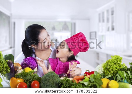 Asian mother is teaching her daughter to cut vegetable at home