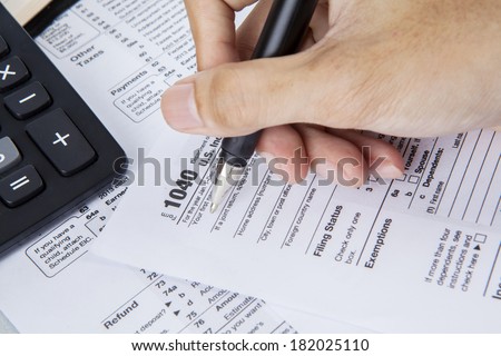 Person completing 1040 tax form with calculator and pen