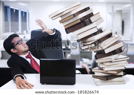 Stress businessman and falling books at office with PC and laptop