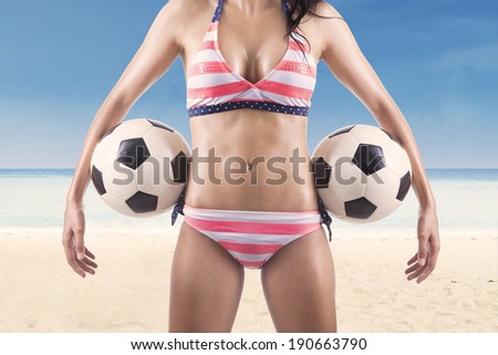 Beautiful body of female soccer fan wearing bikini while holding soccer balls at beach