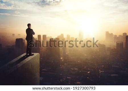 Confident businessman standing on the building rooftop while looking at the silhouette of cityscape at dusk time