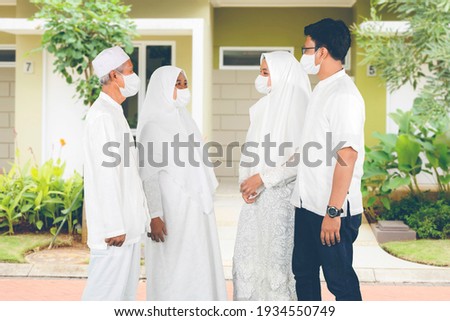 Happy Muslim old couple wearing face mask while chatting with their children on house yard. Shot at Ied Mubarak celebration Imagine de stoc © 