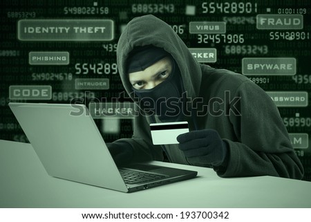 Internet Theft - a man wearing a balaclava and holding a credit card while sat behind a laptop,