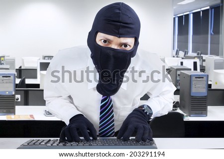 Computer hacker - businessman wearing mask stealing data from computer.