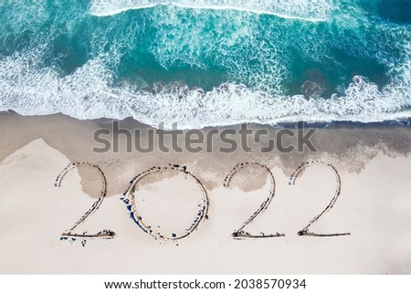 2022 new year concept. Top view of 2022 numbers written on the sand of coastline with frothy waves