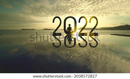 Silhouette of young woman exercising yoga while doing meditation with 2022 numbers on the beach at sunset time