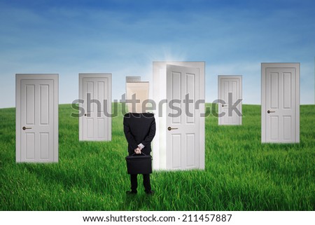 Anonymous businessman standing in front of opportunity doors on the green field