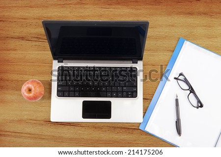 Laptop computer, folder, and apple on a wooden tablet with glasses and a pen