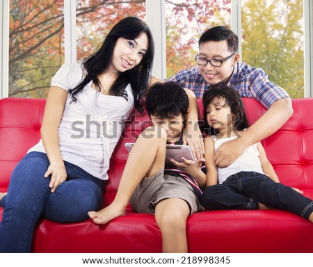 Two hispanic parents with their children on sofa using digital tablet with autumn background on the window