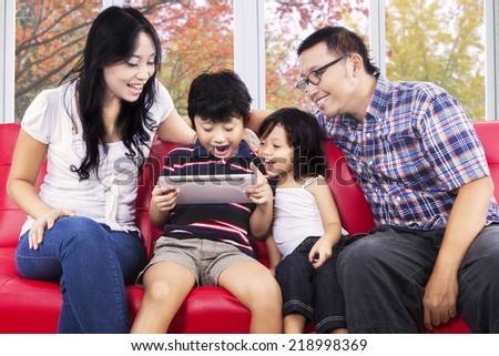 Portrait of cheerful family sharing digital tablet for play game on sofa with autumn background