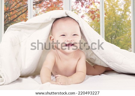 Baby lying under blanket and laughing alone with autumn tree background