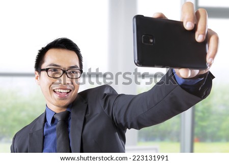 Asian businessman taking self portrait with smartphone in office