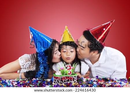 Portrait of two asian parents kiss their daughter when she blowing the candle on birthday cake