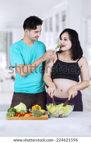 Portrait of asian husband giving healthy food to his pregnant wife in the kitchen