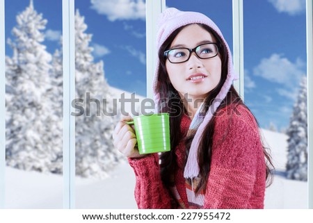 Beautiful young asian girl wearing warm clothes while drinking hot beverage at home in winter day