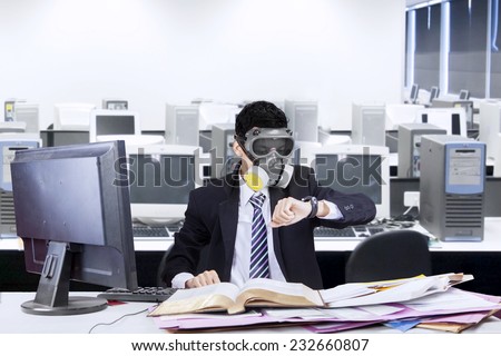Businessman working in office with a gas mask and looking at his watch