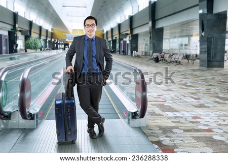Young businessman in formal suit carrying briefcase and luggage while standing in the airport hall