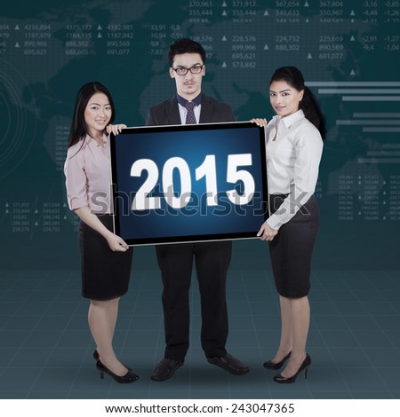 Group of multi ethnic businesspeople holding a board with numbers 2015 in front of financial background