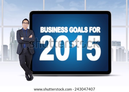 Young businessman standing in the office while leaning on a board of business goals for number 2015