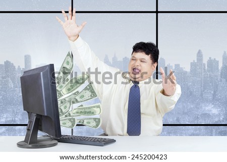 Happy male entrepreneur celebrate his success while working on computer and get money