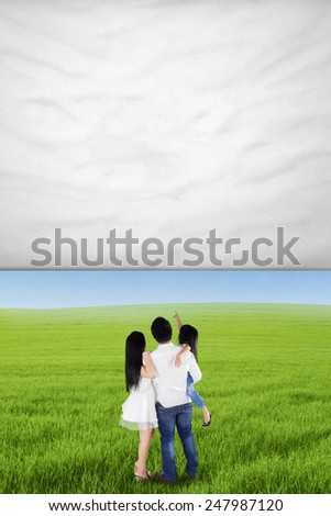Back view of happy family standing on the meadow while looking at empty banner