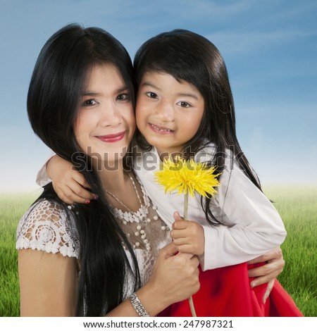 Portrait of happy child smiling at the camera while holding a flower with her mother
