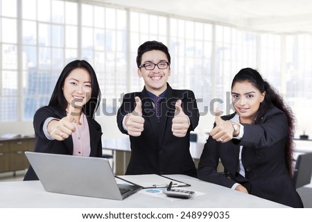 Group of multiracial business team showing thumbs up and smiling at the camera in the office