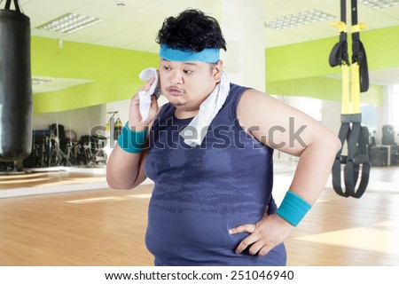 Exhausted man after workout and wiping his sweat at gym