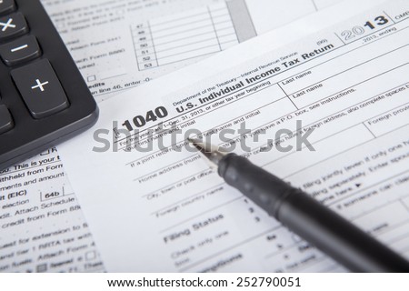 Closeup of a pen pointing at tax form with calculator, symbolizing the time to pay tax