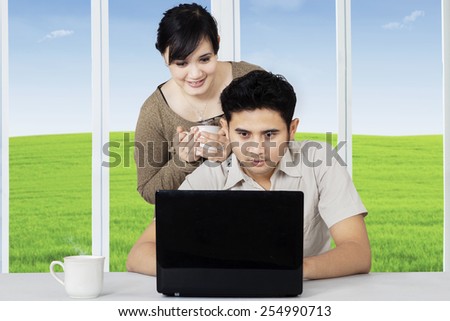 Young asian couple using laptop computer to surf internet online while enjoy hot drink