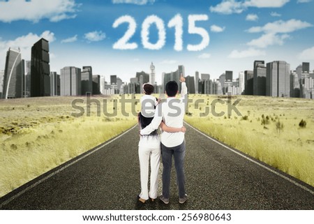 Back view of happy family standing on the road while pointing at numbers 2015 over the city