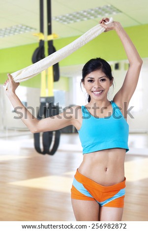 Young fitness woman standing in the fitness center while smiling at the camera and holding a towel
