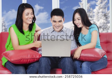Happy people sitting on sofa while using a laptop computer to browse internet online at home