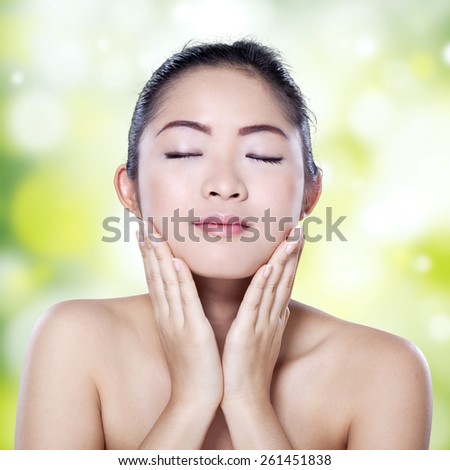 Portrait of young chinese girl with soft beauty skin touching her face against bokeh light background