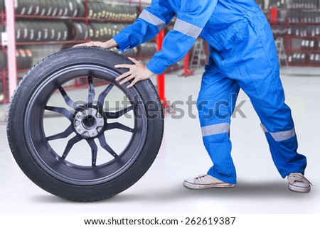 Male technician with a blue clothes changing a tire in the workshop