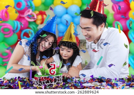 Lovely family celebrating birthday party and cutting a birthday cake together with colorful balloons background