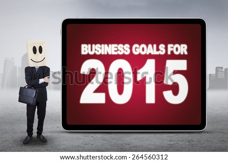 Male entrepreneur with a carton head and smiley face, standing next to the board of business goals for 2015