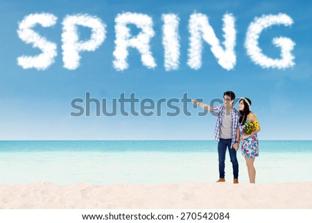 Young couple walking on the beach with cloud shaped a spring text