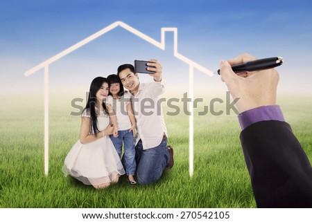 Little happy family taking self photo together on the meadow under a dream home