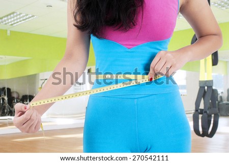 Female fitness trainer use a measurement tape to measure her belly at fitness center