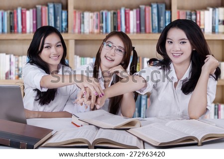 Portrait of three high school students joining hands together in the library
