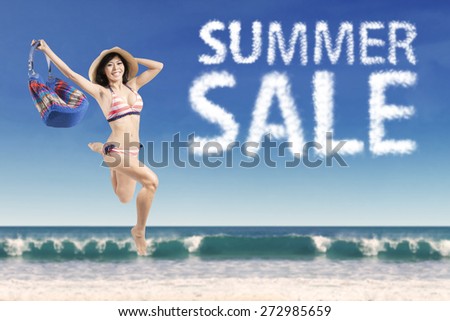 Beautiful female model wearing bikini and jumping at beach with summer sale cloud